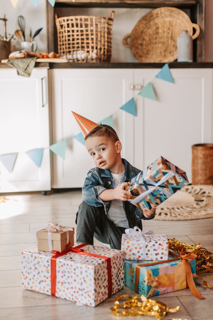 gallery-2 A child enjoying a birthday celebration with colorful presents and a party hat indoors.